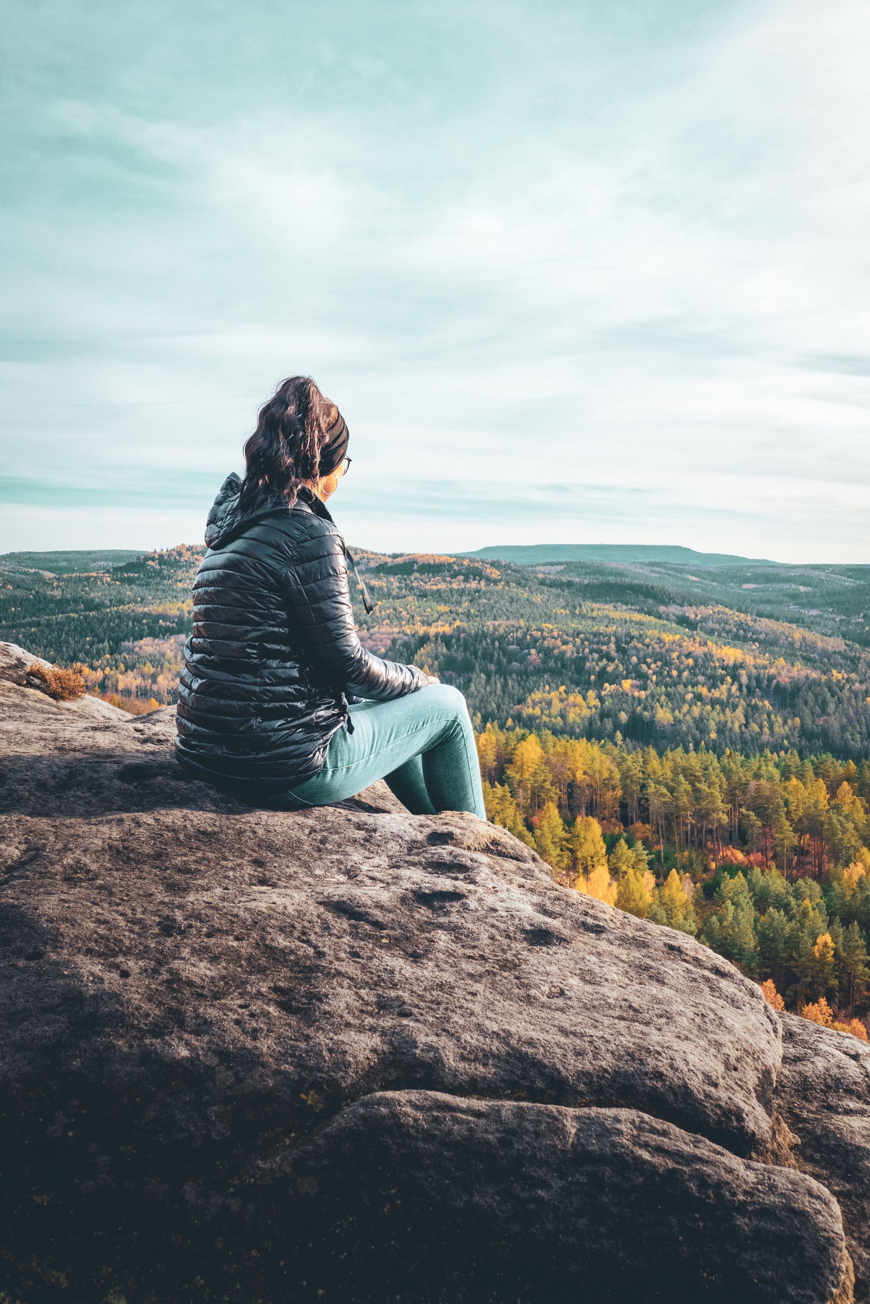A woman sits on a cliff in Saxon Switzerland, enjoying a scenic autumn view.