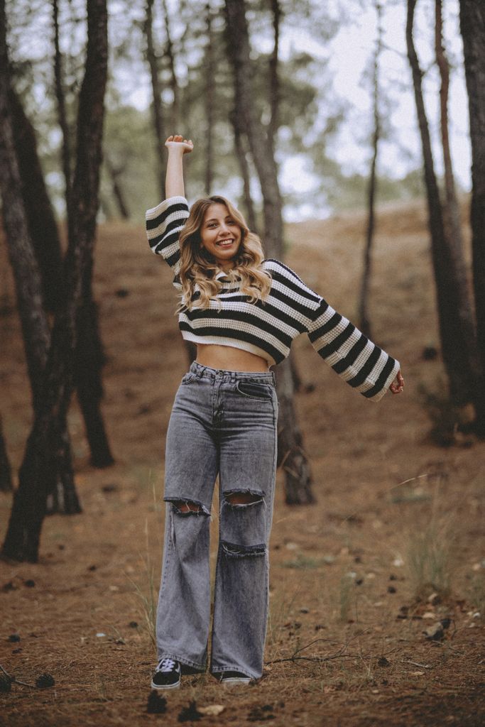 Smiling young woman in casual outfit enjoying a peaceful walk in a wooded area during autumn.