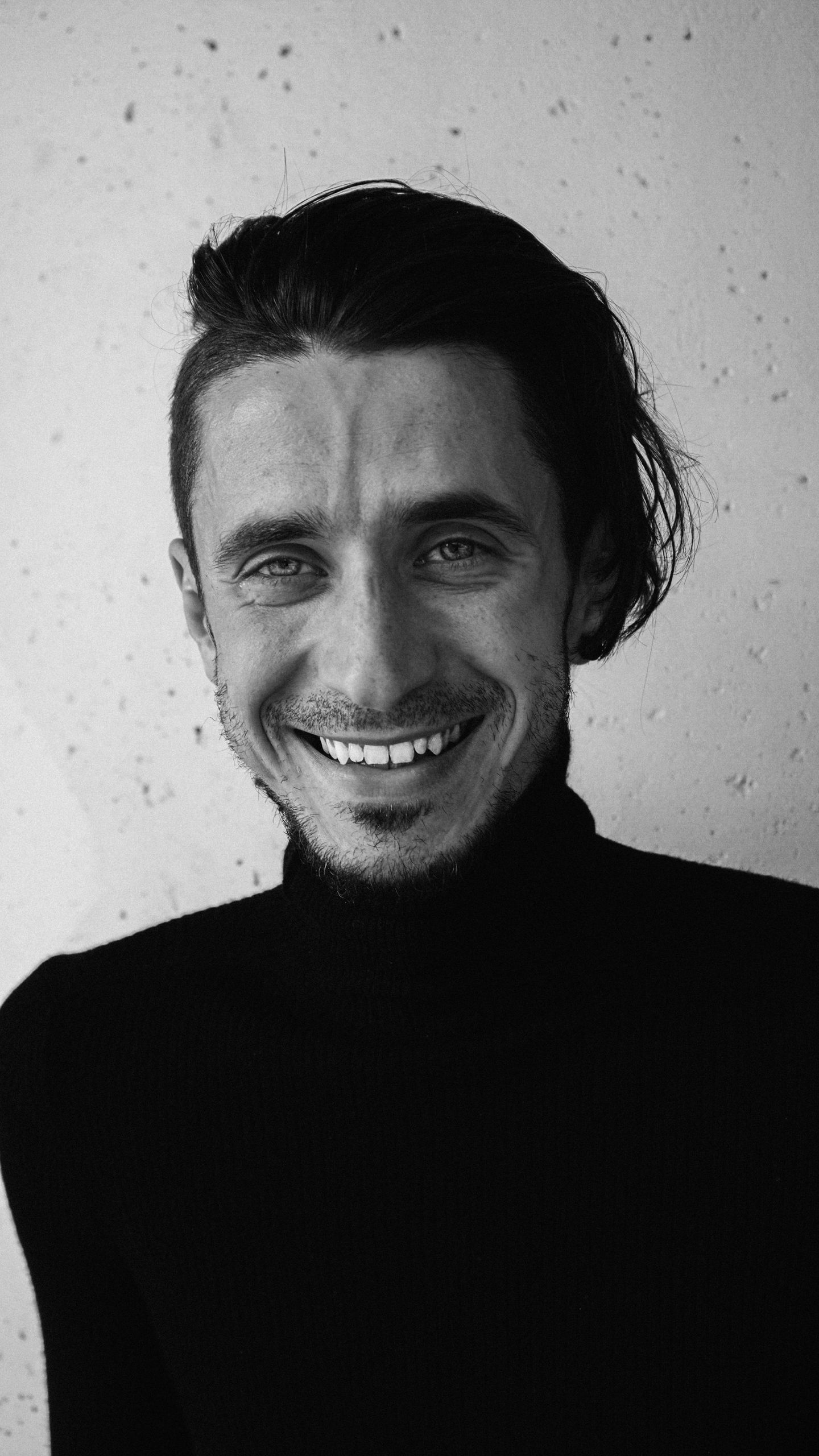 Monochrome portrait of a smiling man in a turtleneck, exuding warmth and charisma.